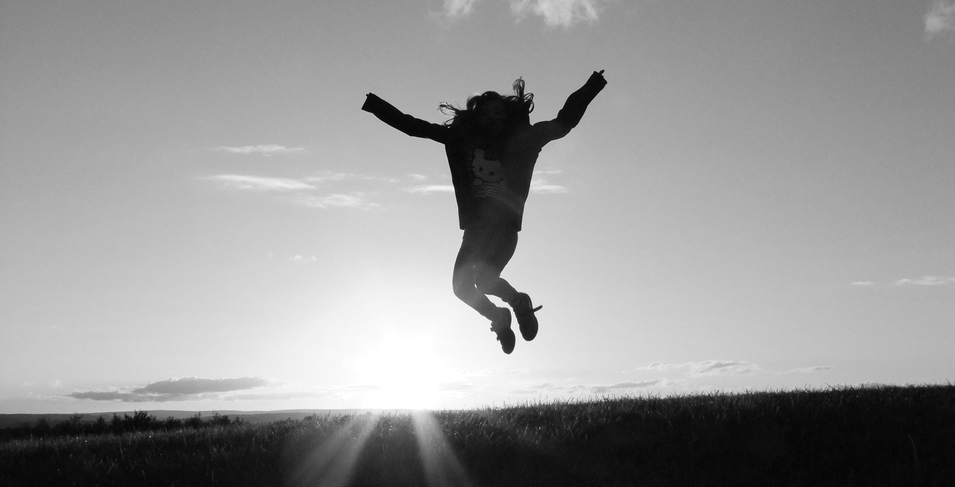 Person springt in die Luft, im Hintergrund der Horizont mit untergehender Sonne